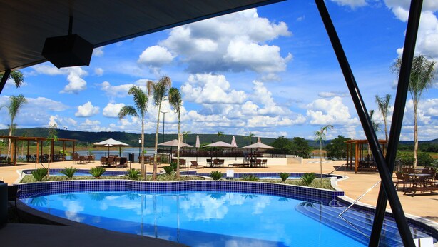 A swimming pool with blue tiles, surrounded by palm trees and outdoor seating areas. - Praias do Lago Eco Resort by WAM Experience (Caldas Novas)