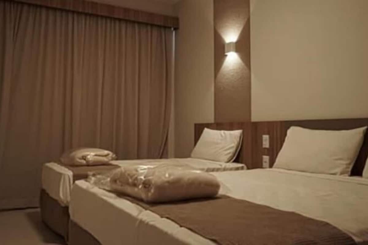 A hotel room with two beds, a large window with curtains, and a wall-mounted light fixture.