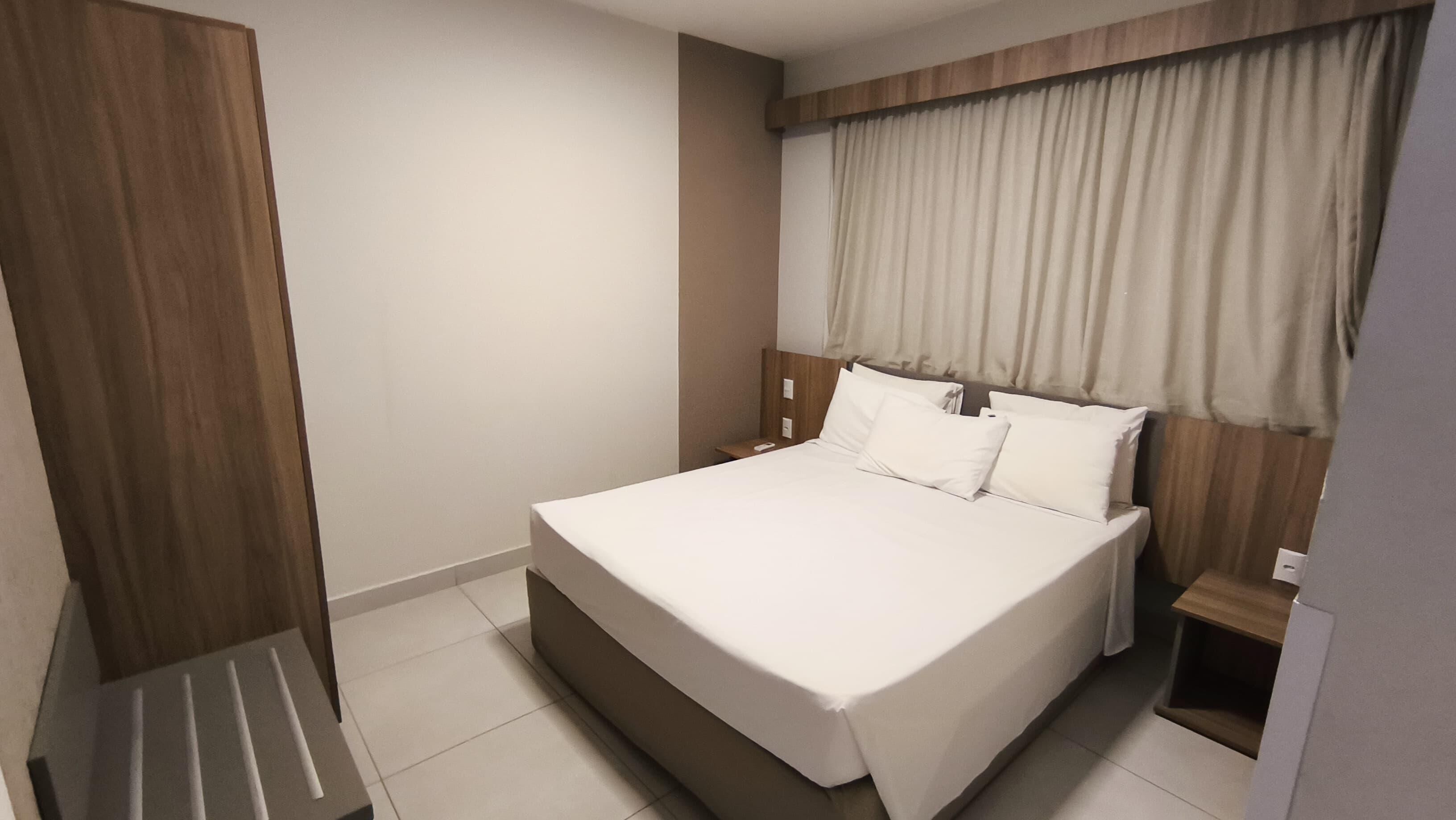 A modern hotel room with a large bed, wooden headboard, and a small bedside table.