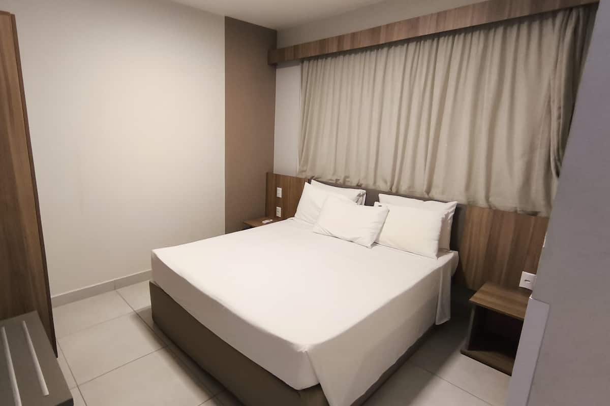 A modern hotel room with a large bed, wooden headboard, and a small bedside table.