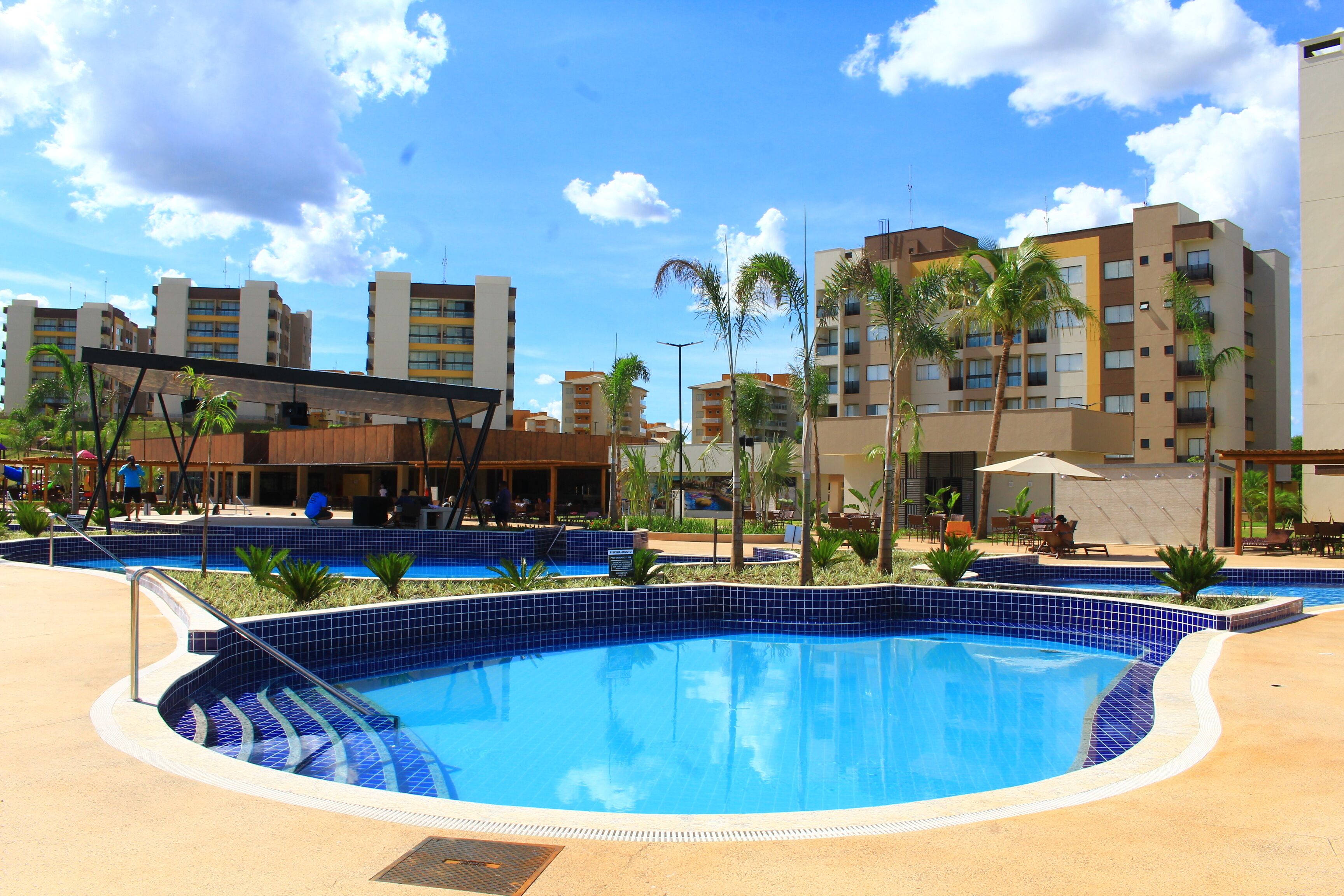 A swimming pool with tiled edges, surrounded by palm trees and buildings.