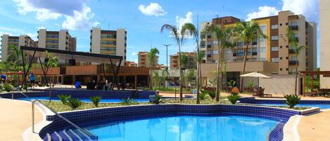A swimming pool with tiled edges, surrounded by palm trees and buildings.