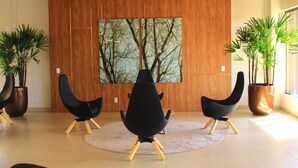 A modern interior with three black chairs on a light-colored rug, wooden panel walls, and large potted plants. - Praias do Lago Eco Resort by WAM Experience (Caldas Novas)