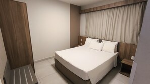 Ein modernes Hotelzimmer mit einem großen Bett, einem Holzkopfteil und einem Fenster mit Vorhängen.