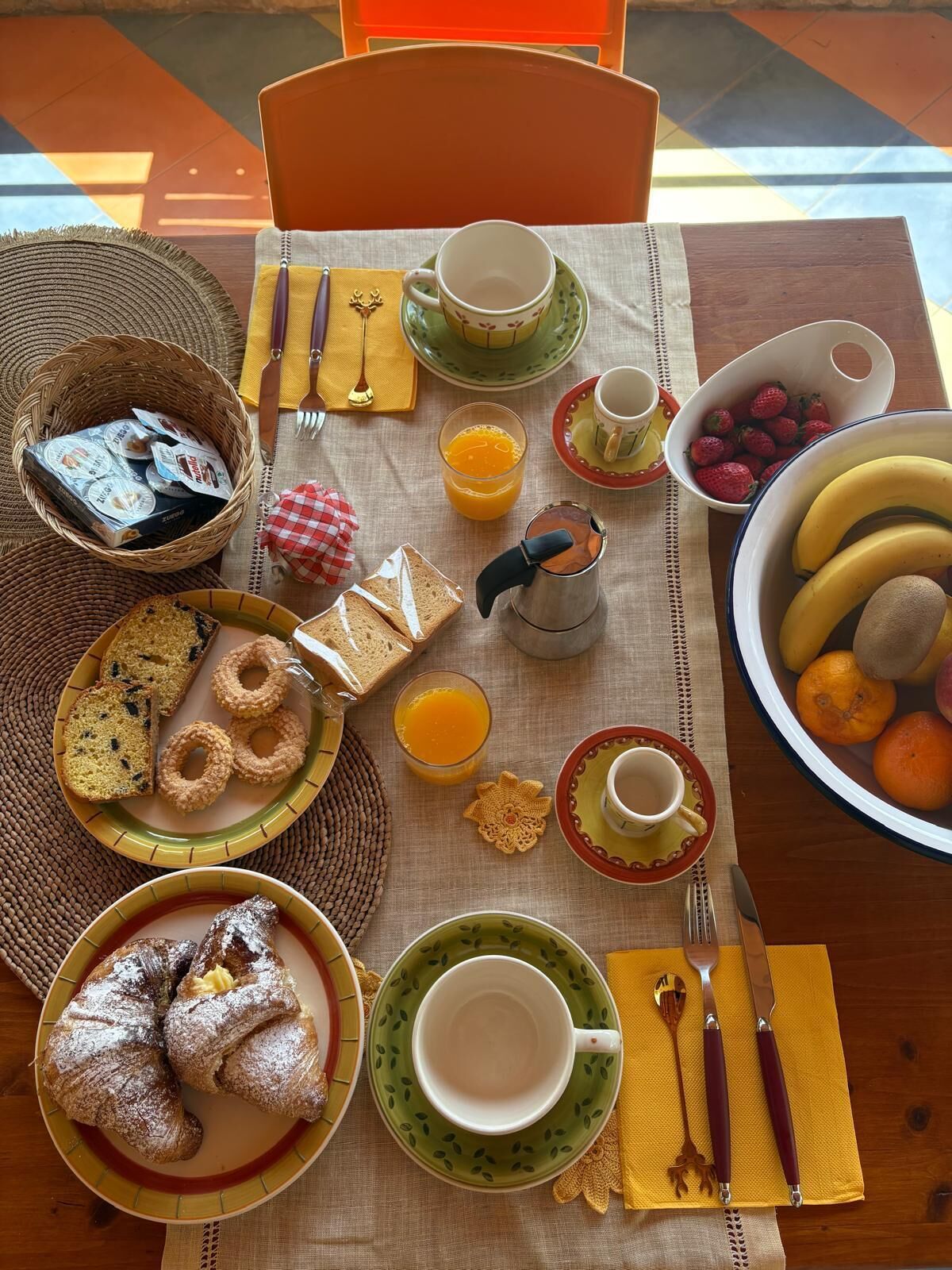 A breakfast setting with various food items, utensils, and a tablecloth.