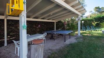 Un espace extérieur abrité comprenant une table de ping-pong, des chaises et une structure de jeu jaune.