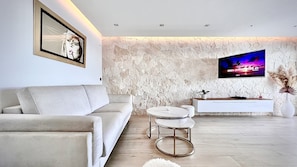 A modern living room with a stone wall, a mounted TV, a sofa, a small round table, and a white console.