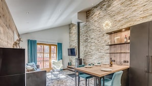 A modern living room with a stone wall, a dining area with a wooden table, and a black cabinet.