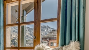 A fluffy chair in a room with a large window, a wooden door, and a view of a mountainous landscape.