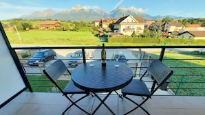 Un balcón con una mesa redonda y cuatro sillas, con vistas a una zona residencial con casas y montañas al fondo.