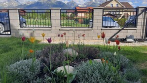 Un jardín con diversas flores y plantas, un muro de piedra y una vista de montañas al fondo.