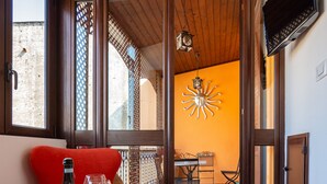 Una habitación con suelo de madera, una mesa con una botella y un vaso, una silla roja y vistas a un área exterior con mesa y sillas a través de una puerta abierta.