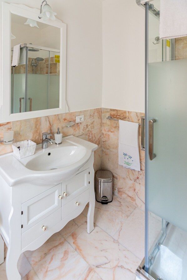 A bathroom with a white sink, mirror, and marble-tiled walls.