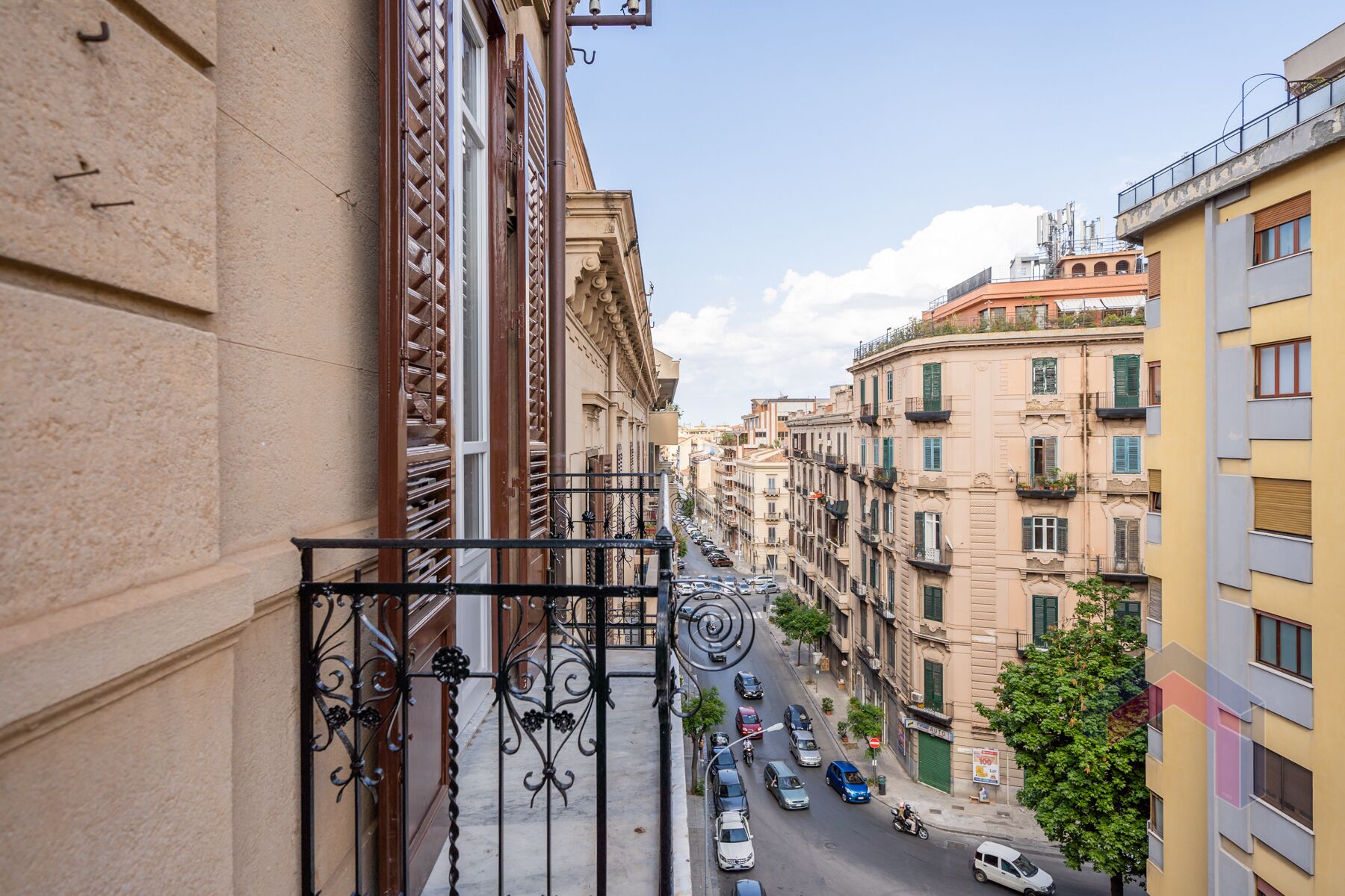 A street view from a balcony with buildings on either side, featuring balconies with metal railings and a clear sky.