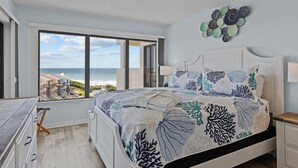 A bedroom with a large window offering a view of the beach and ocean. - The Beach Hive: Ocean view condo in the heart of Emerald Isle (Emerald Isle)