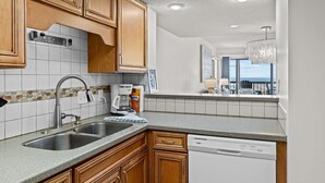 A modern kitchen with wooden cabinets, a double sink, and a dishwasher. - The Beach Hive: Ocean view condo in the heart of Emerald Isle (Emerald Isle)