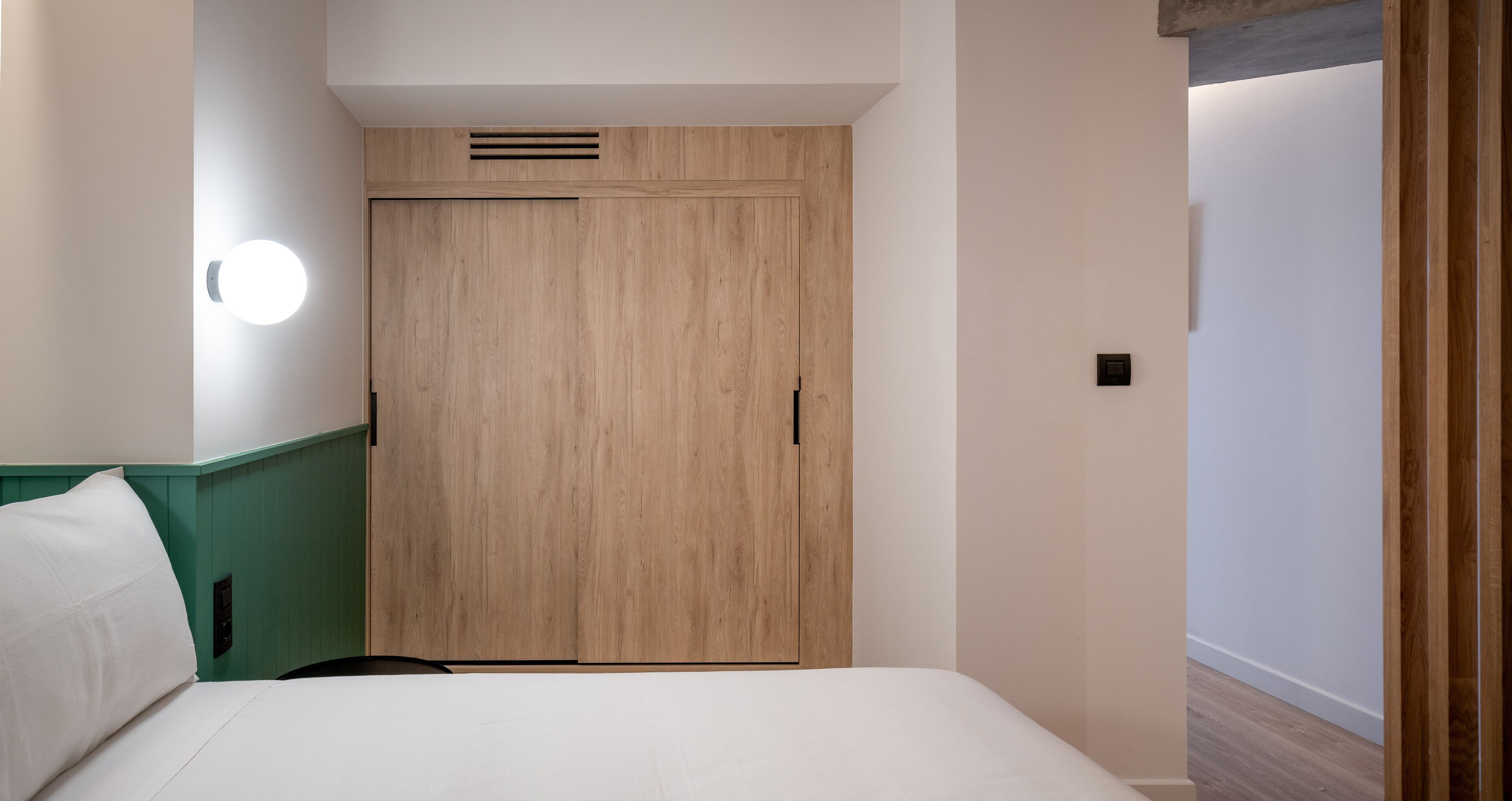 Een hotelkamer met een bed, een houten kledingkast, een wandlamp en een groene accentmuur.