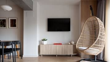 Un soggiorno moderno con una TV a schermo piatto, un'area pranzo con un tavolo e sedie nere, una poltrona in vimini e un mobiletto in legno con una pianta.