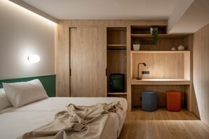 A bedroom with a bed, a wardrobe, a desk with a lamp, and storage units.