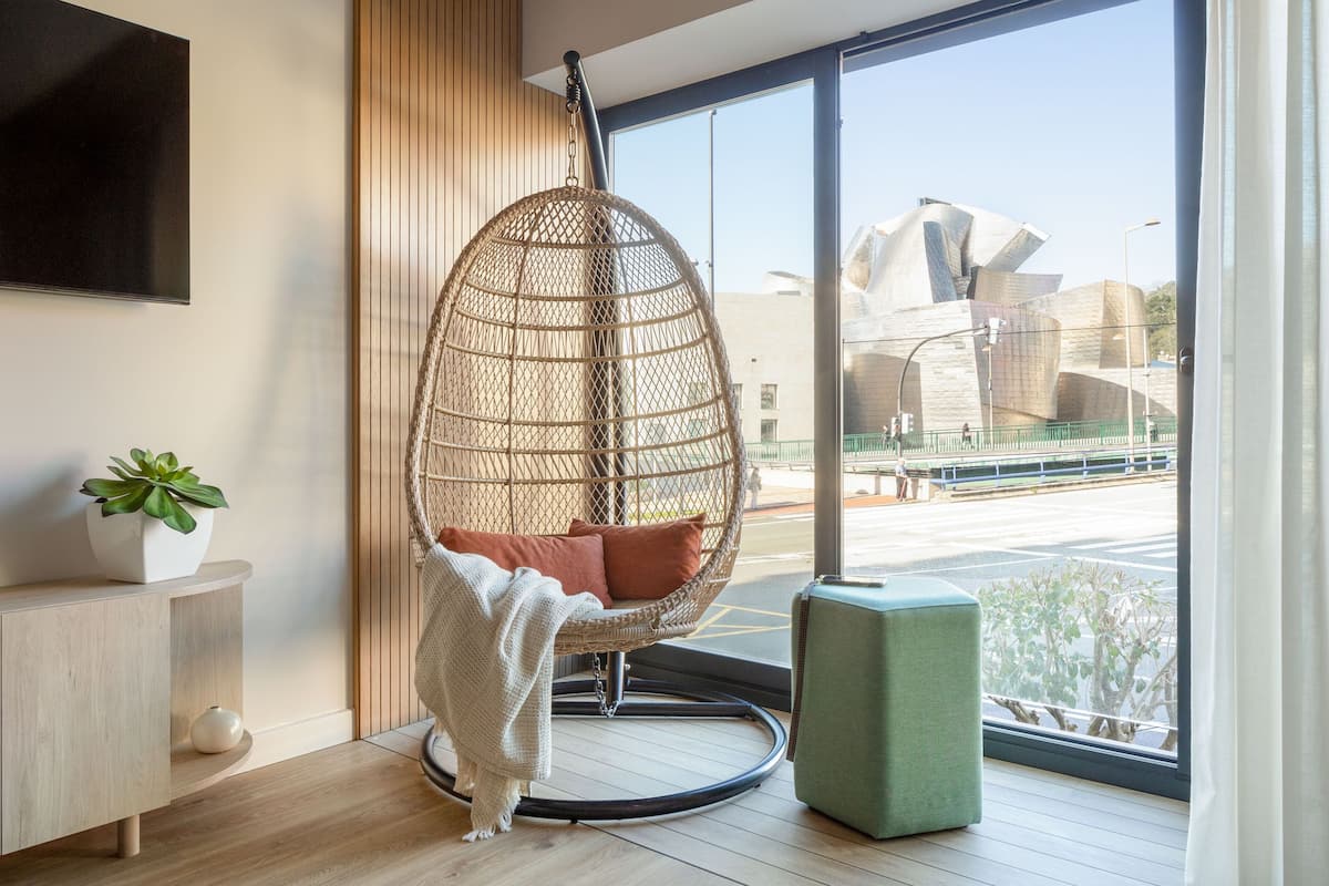 Una habitación moderna con una silla colgante, una planta en maceta y vistas a un edificio famoso.