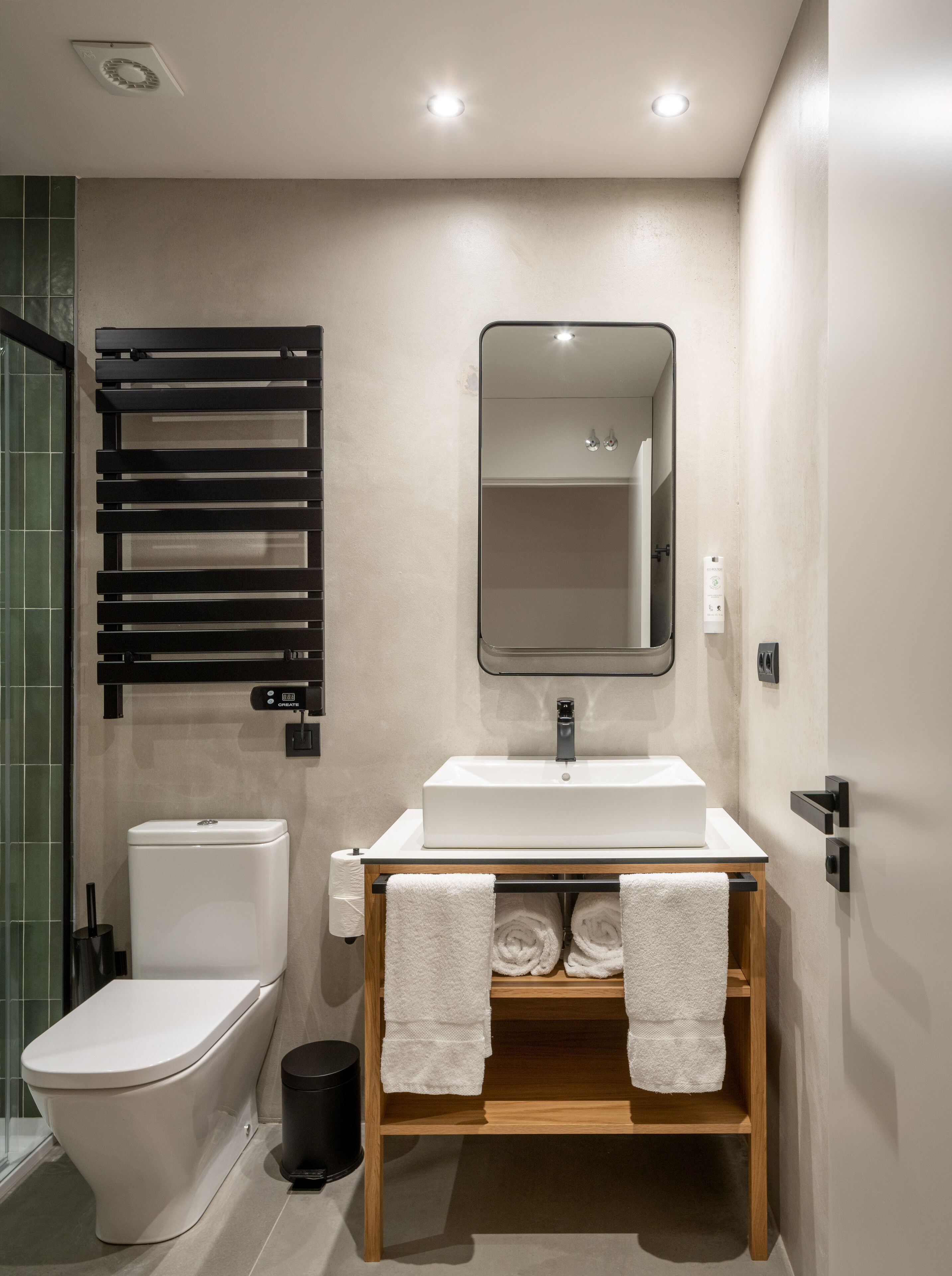 Une salle de bain moderne comprenant des toilettes, un lavabo, un miroir, un porte-serviettes et un espace douche.