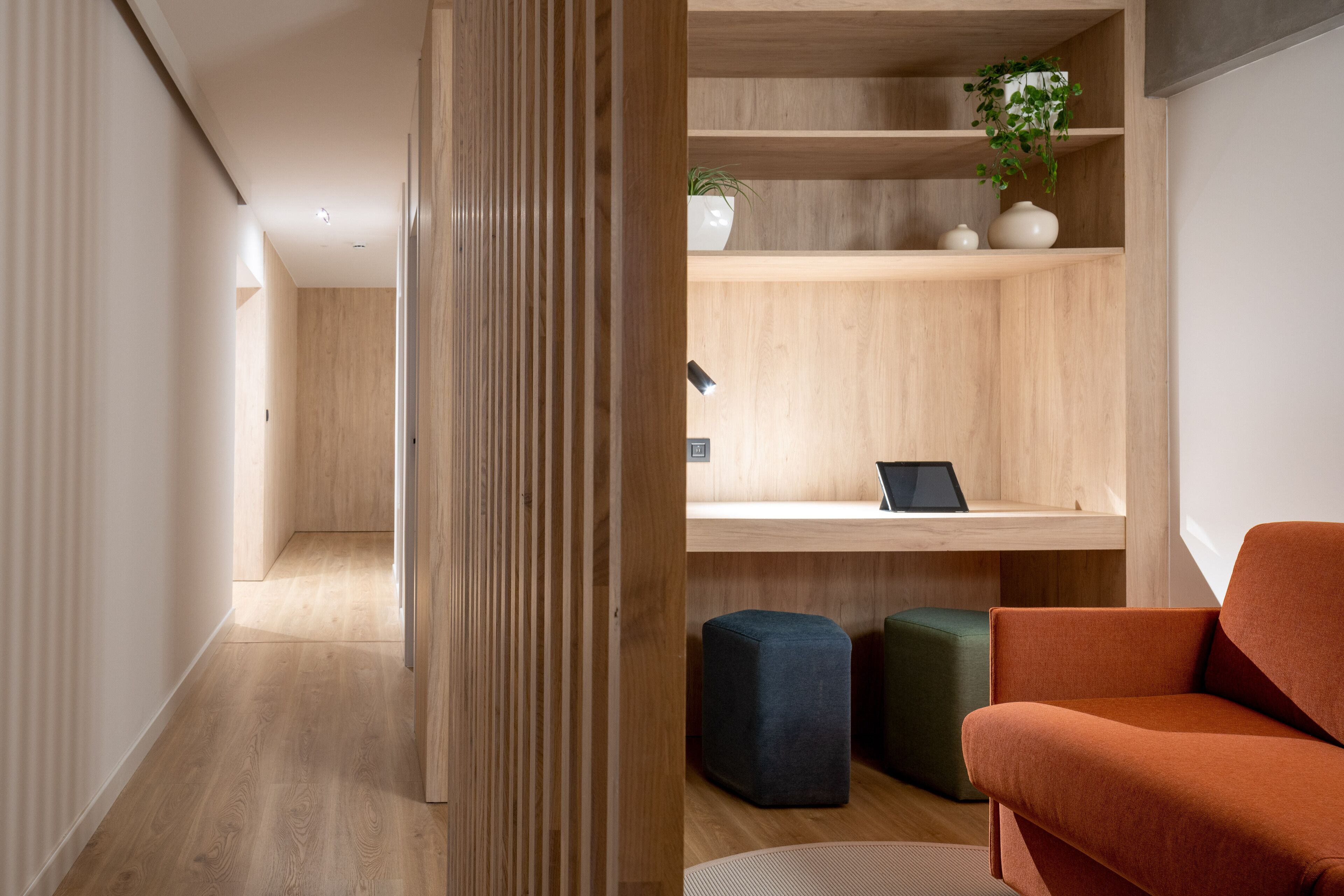 Un intérieur moderne avec un plancher en bois, un bureau avec un ordinateur portable, un pouf vert et une chaise orange.
