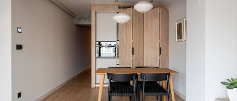 A modern dining area with a wooden table and chairs, a light fixture, and a view into the kitchen.