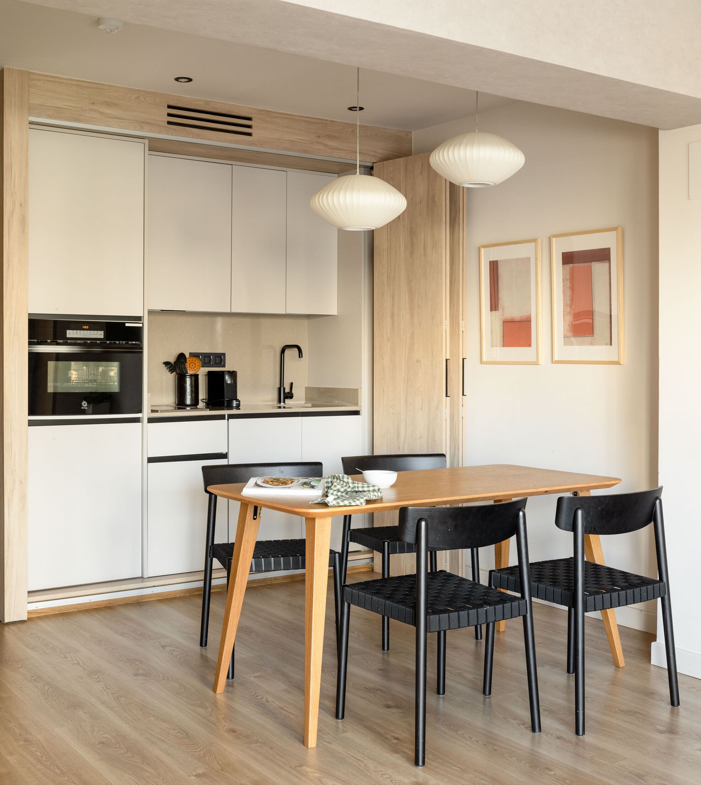 A compact kitchen with modern appliances, a dining table with chairs, and pendant lighting.