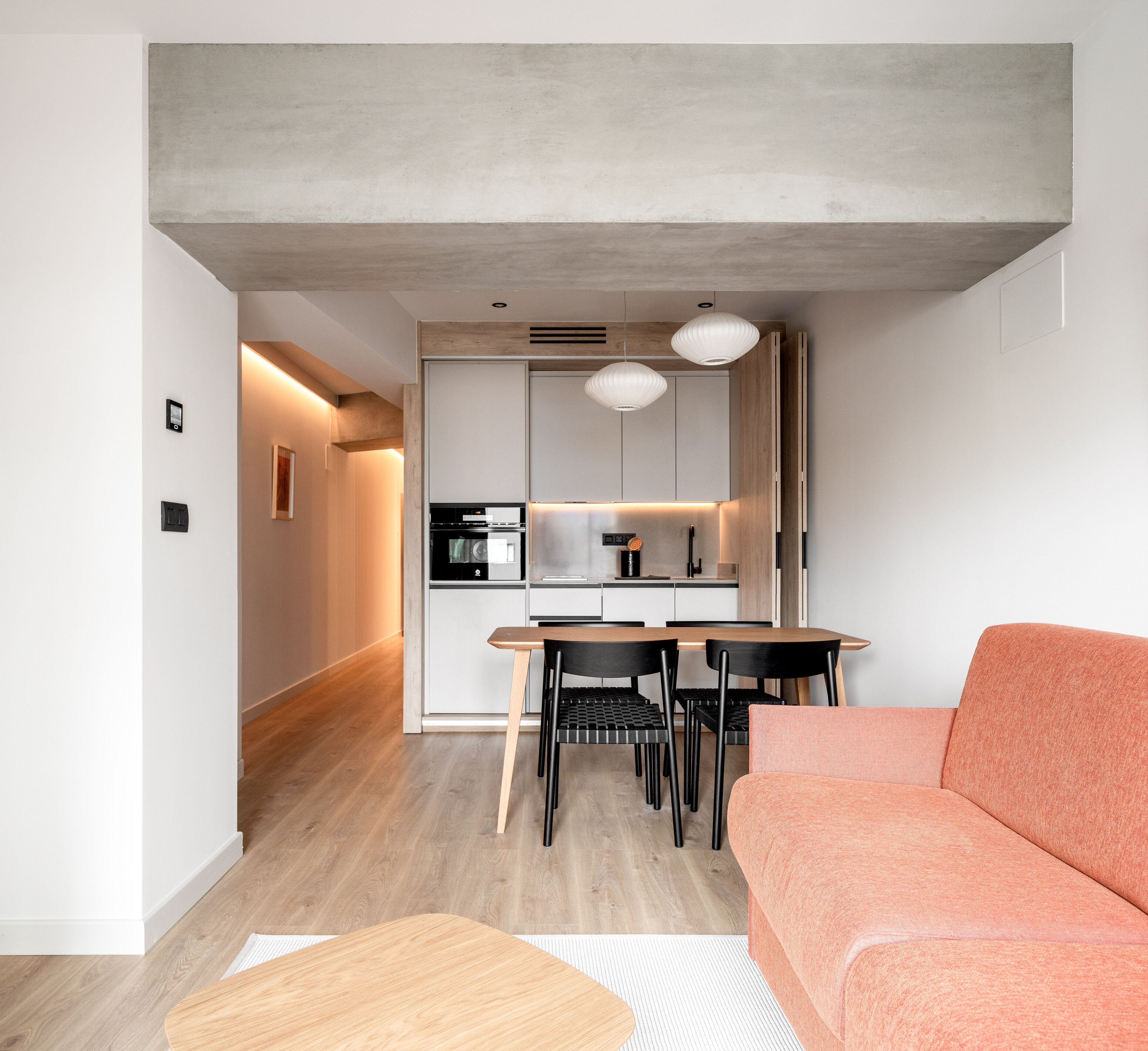Une cuisine moderne avec des meubles blancs, une table à manger et des chaises noires. On trouve un canapé rose dans l’espace salon.