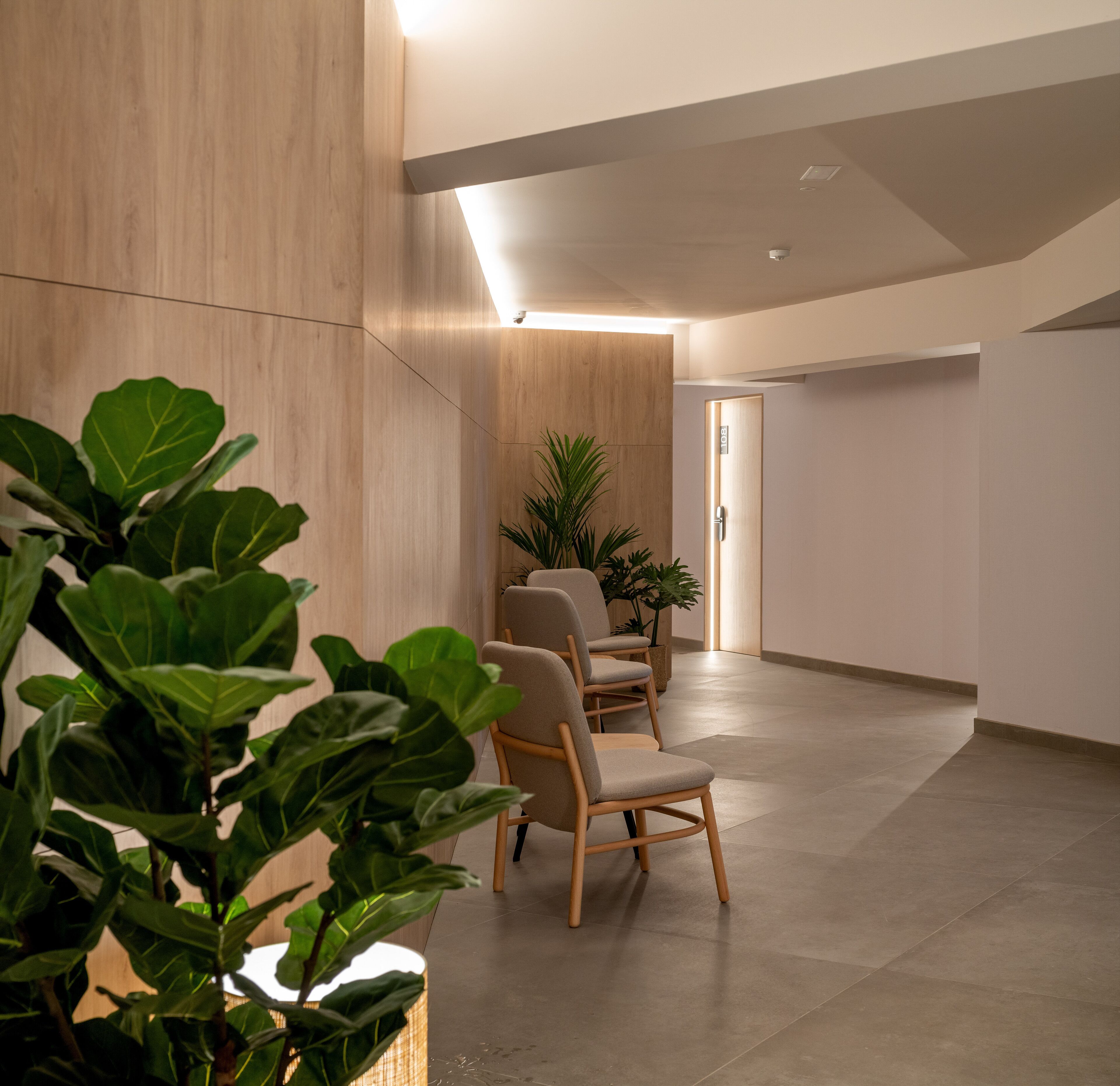 Un espace d’attente moderne avec des murs lambrissés en bois, un coin salon avec des chaises et des plantes en pot.