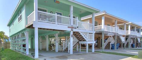 A two-story building with a green exterior and white railings, featuring multiple balconies and a central staircase.