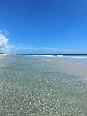 Una playa con aguas transparentes y poco profundas, y una costa distante.