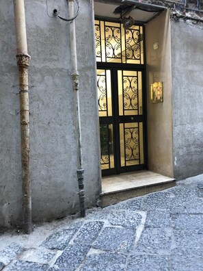 A building entrance with a metal gate, a concrete wall, and a tiled pavement. - Apartment in the center of Naples (napoli)