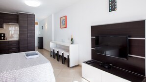 Habitació d'hotel moderna amb llit, televisió, petita cuina i zona de seients.