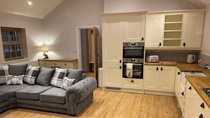 A modern kitchen with white cabinets, a grey sectional sofa, and a wooden floor. - 3 bedroom accommodation in Stalmine, near Poulton-le-Fylde (Stalmine, near Poulton-le-Fylde)