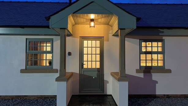 A house with a dark entrance, two windows with lights, and a gravel driveway. - 3 bedroom accommodation in Stalmine, near Poulton-le-Fylde (Stalmine, near Poulton-le-Fylde)