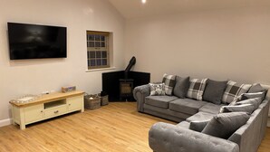 A living room with a grey sofa, a flat-screen TV, a wooden cabinet, and a fireplace. - 3 bedroom accommodation in Stalmine, near Poulton-le-Fylde (Stalmine, near Poulton-le-Fylde)