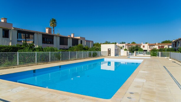 Une piscine rectangulaire à l’eau d’un bleu limpide, entourée d’une terrasse carrelée et d’une clôture en métal.