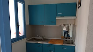 Une cuisine de taille réduite avec des meubles bleus, un évier en acier inoxydable et une planche à découper en bois.