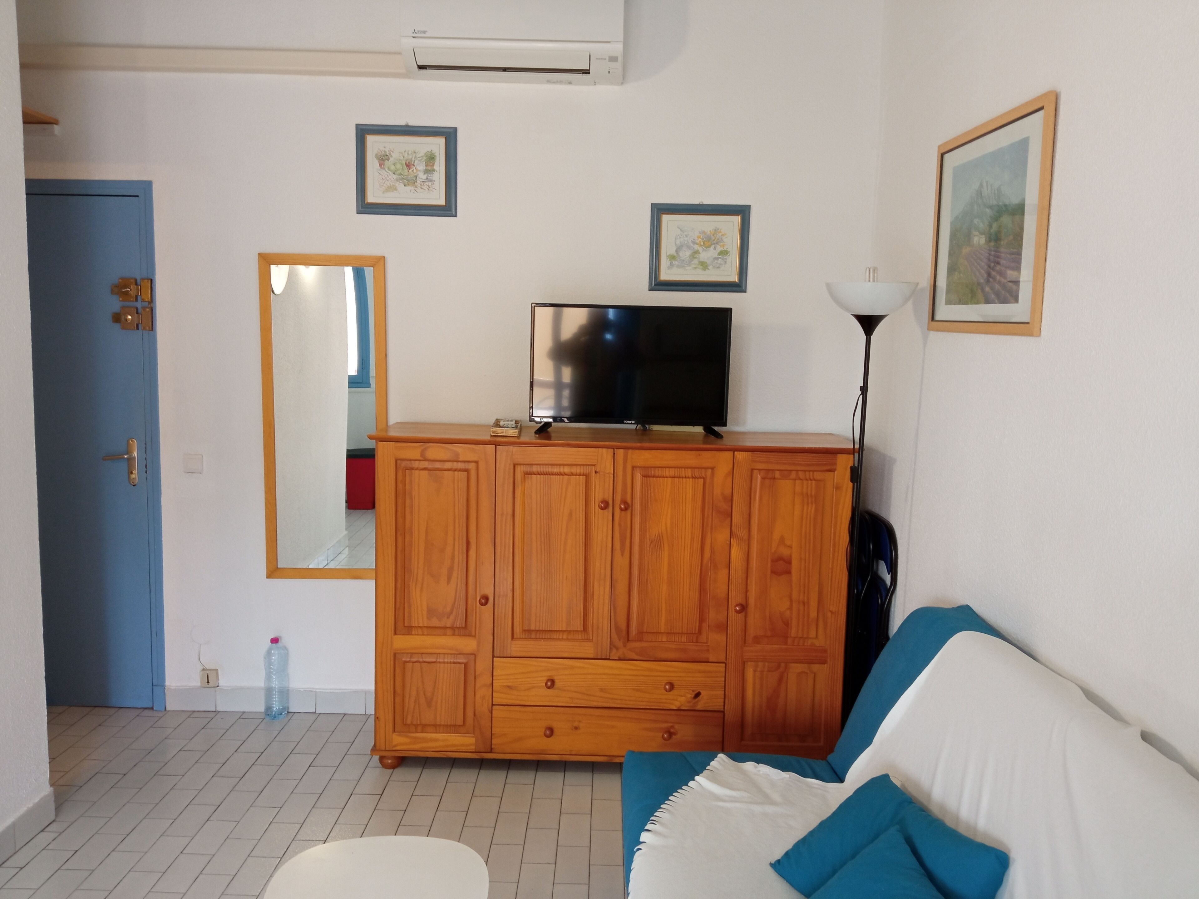 Una habitación con un armario de madera, un televisor, un espejo y una puerta azul.