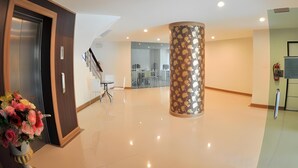A modern hotel lobby with a central column, a staircase, and a reception desk. - The Y Residence (Chiang Mai)