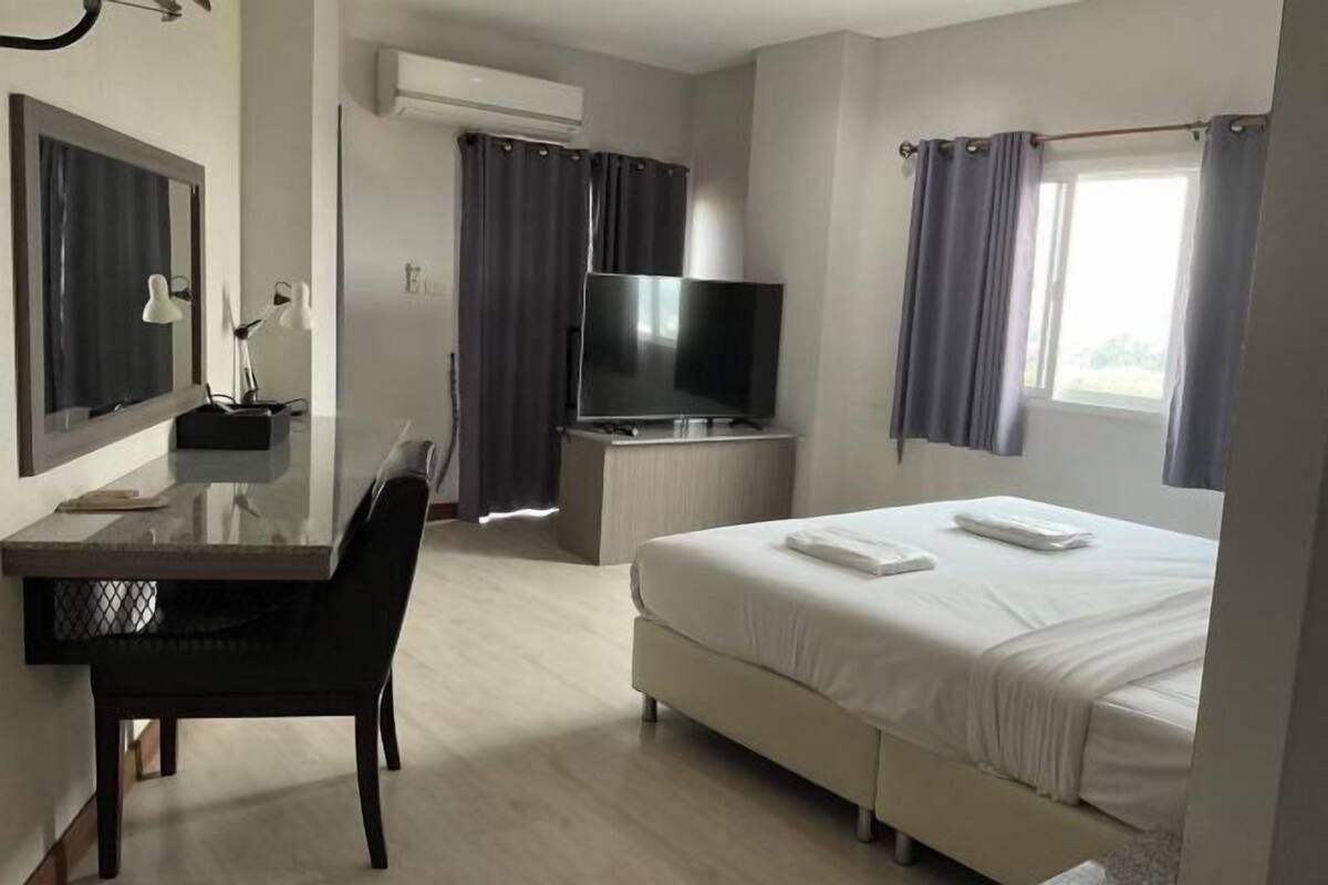 A hotel room with a bed, a desk with a chair, a TV, and a window with curtains.