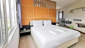 A modern hotel room with a large bed, wooden panel wall, and a small desk with a microwave. - The Y Residence (Chiang Mai)