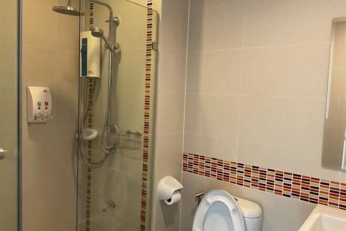A bathroom with a glass shower enclosure, a toilet, and a hand dryer.