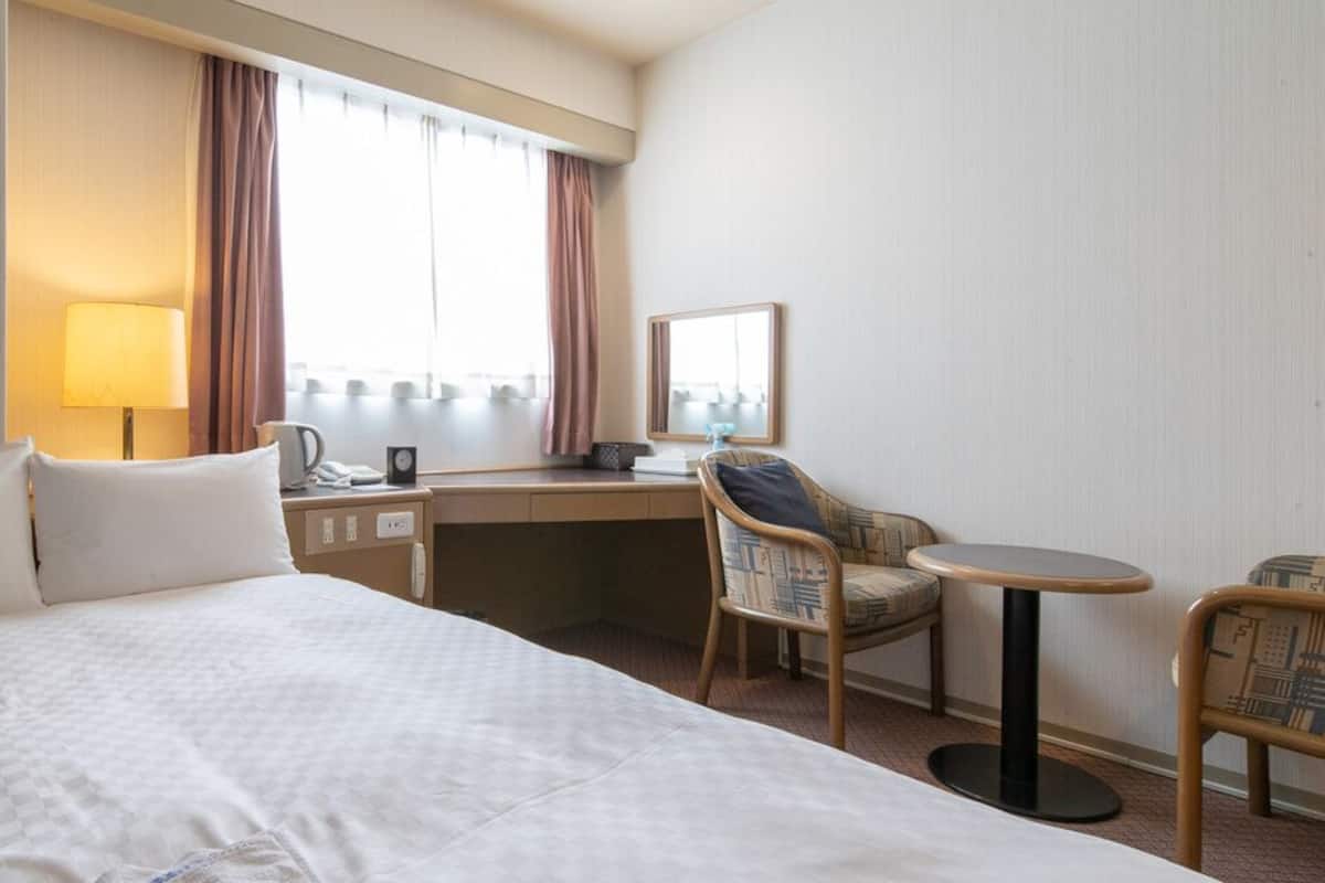 A hotel room with a bed, desk, chair, and a small table.
