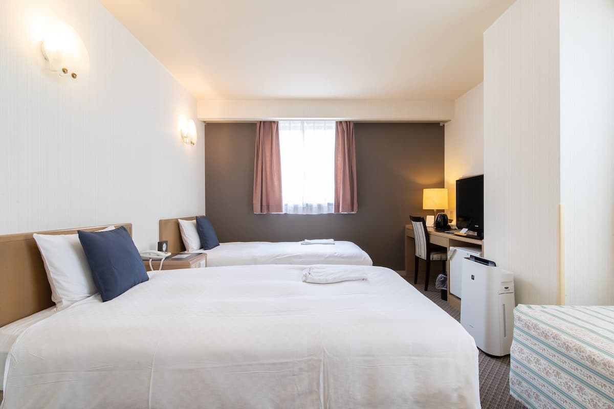 A hotel room with two beds, a desk, a chair, a TV, and a coffee machine.