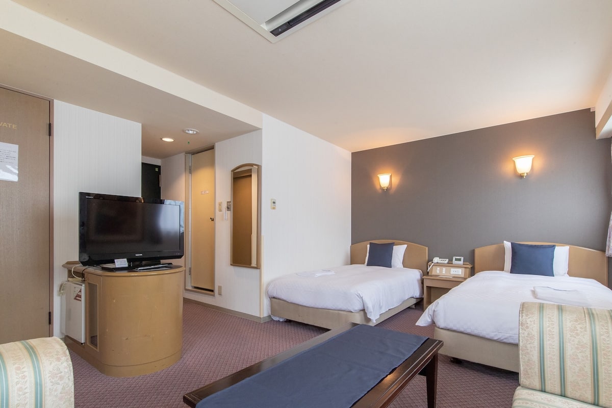 A hotel room with two beds, a TV, a desk, and a sofa.
