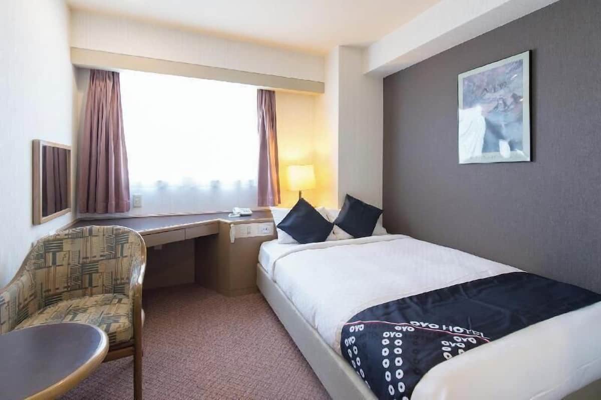 A hotel room with a bed, desk, chair, and a window with curtains.