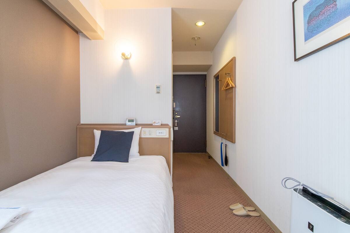 A hotel room with a bed, a bedside table, a wall-mounted TV, and a door leading to another room.