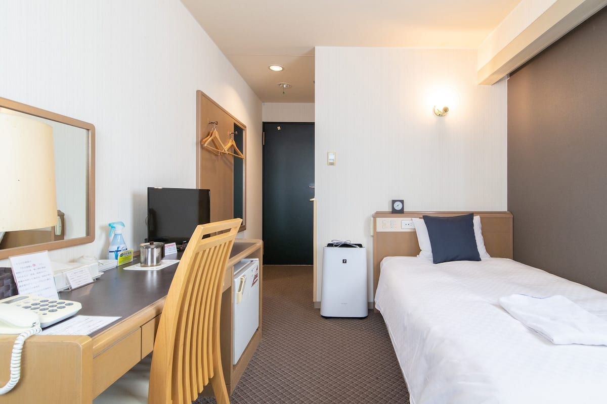 A hotel room with a desk, chair, bed, and a small refrigerator.